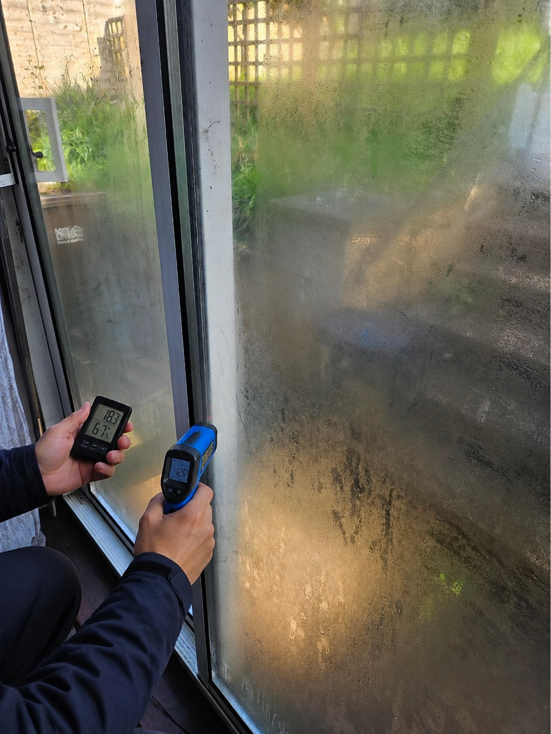 Damp specialist checking humidity and surface temperature beside misted patio doors